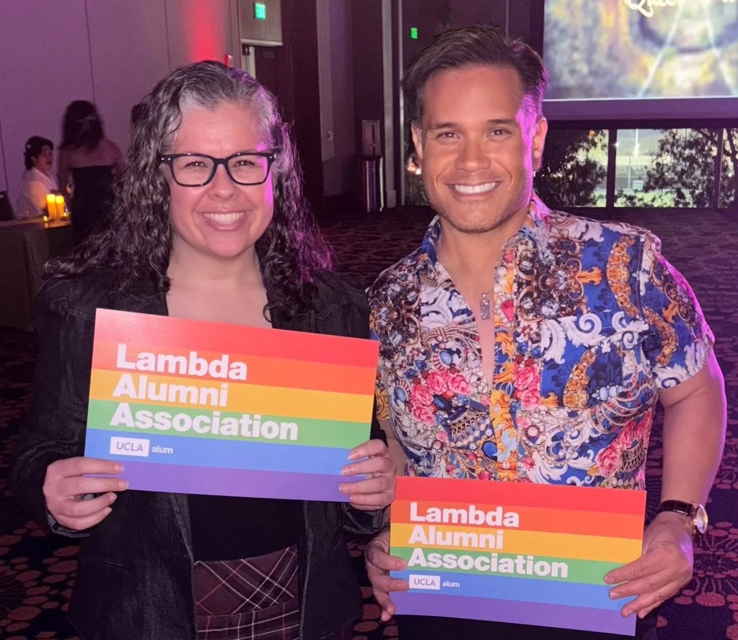 Two people holding small Lambda Alumni Association banners
