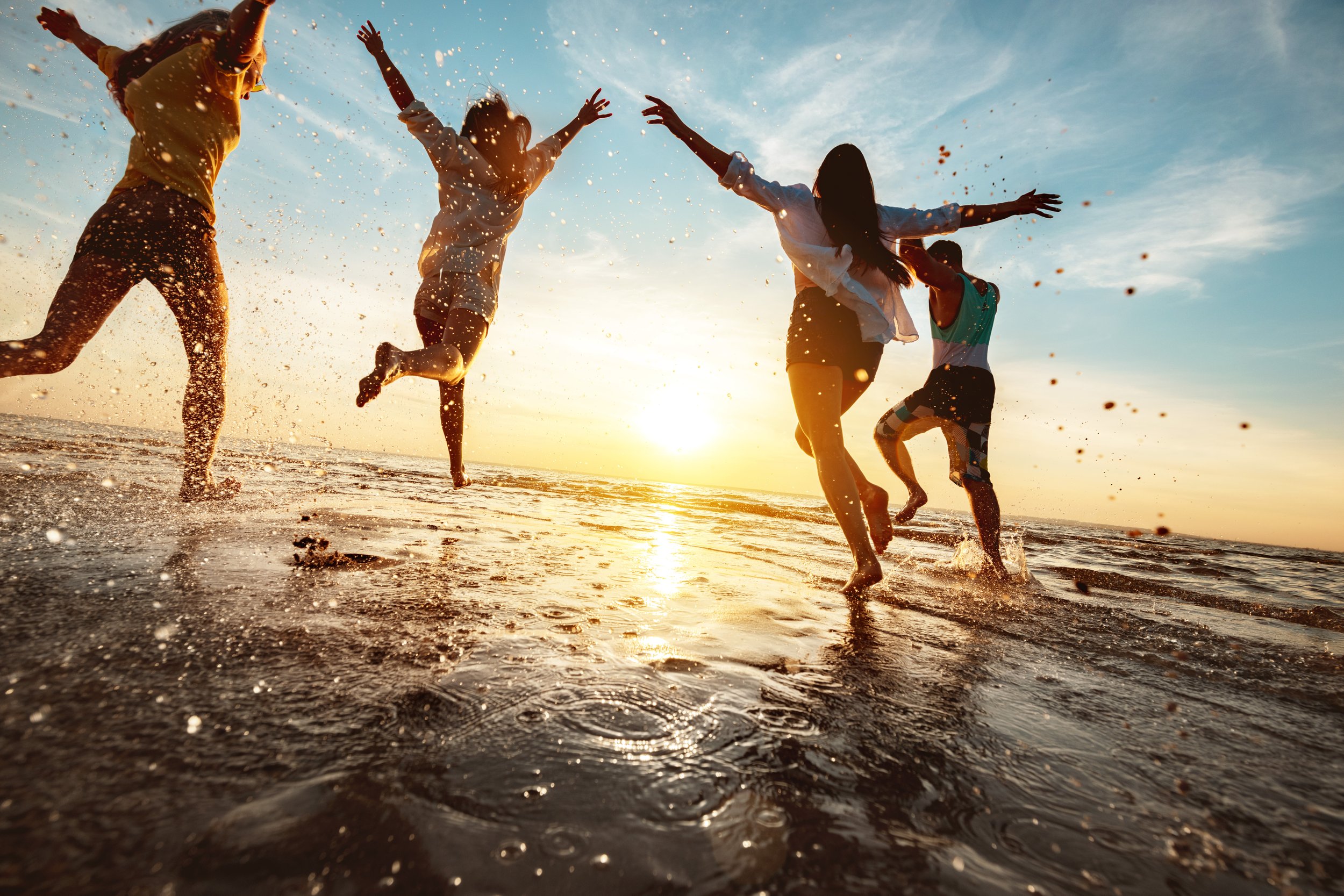 Four people at the beach running into the water at sunset