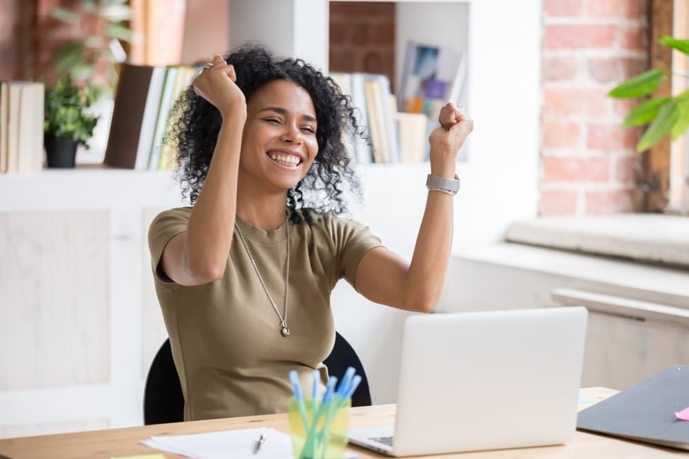 Woman celebrating while sitting at a laptop