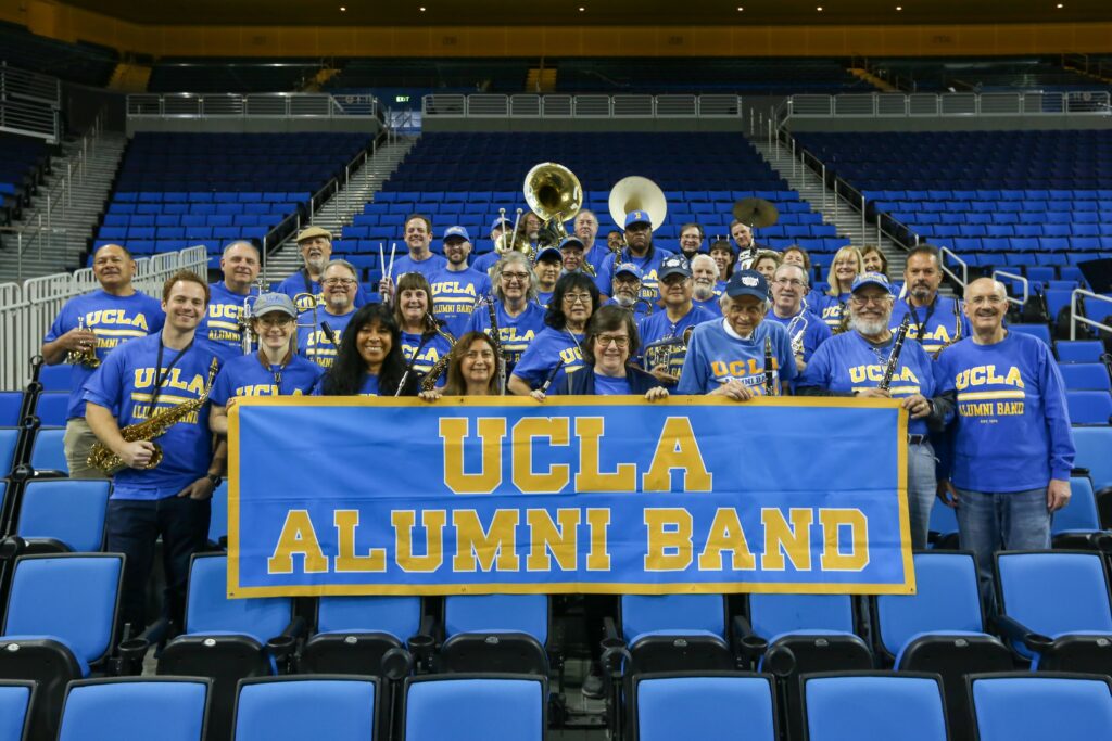 Male and female alumni holding musical instruments and a blue and yellow banner that reads UCLA Alumni Band.