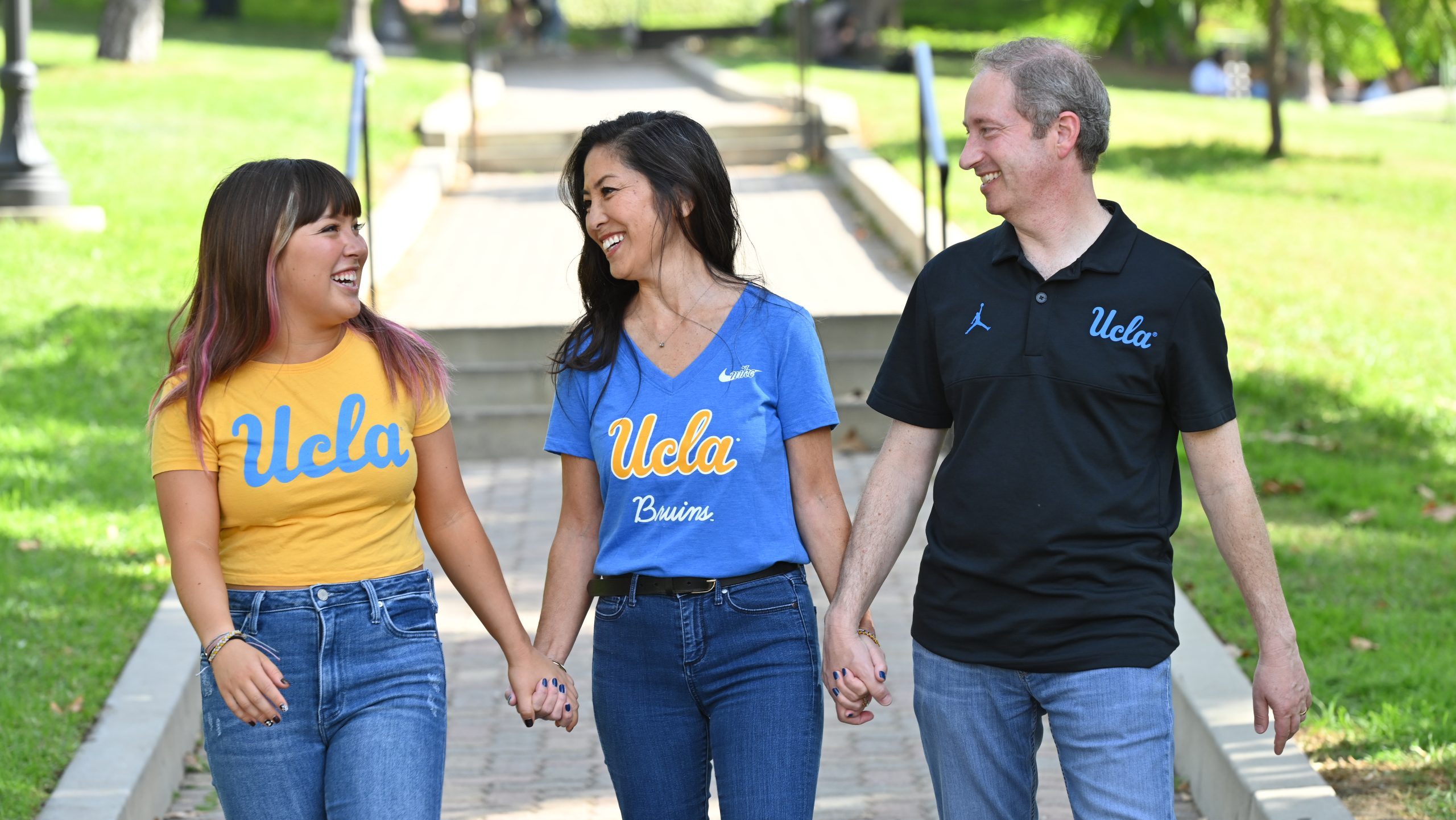 A family of three walk hand in hand in UCLA gear.
