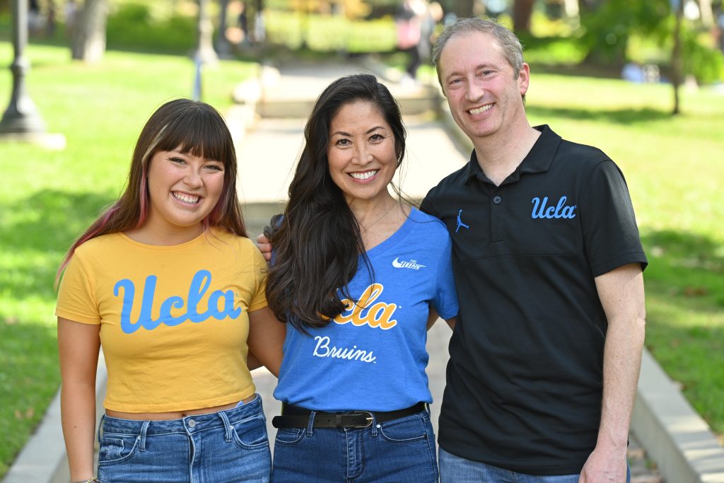A daughter, mother and father wearing UCLA gear smile at the camera with their arms around each other.