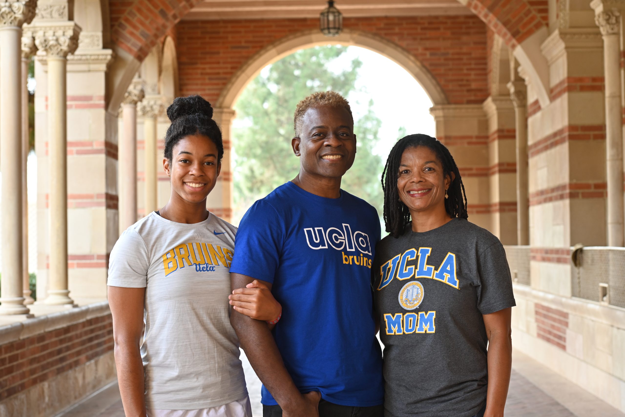 A daughter, father and mother in UCLA gear pose together under the arches of Royce Hall.