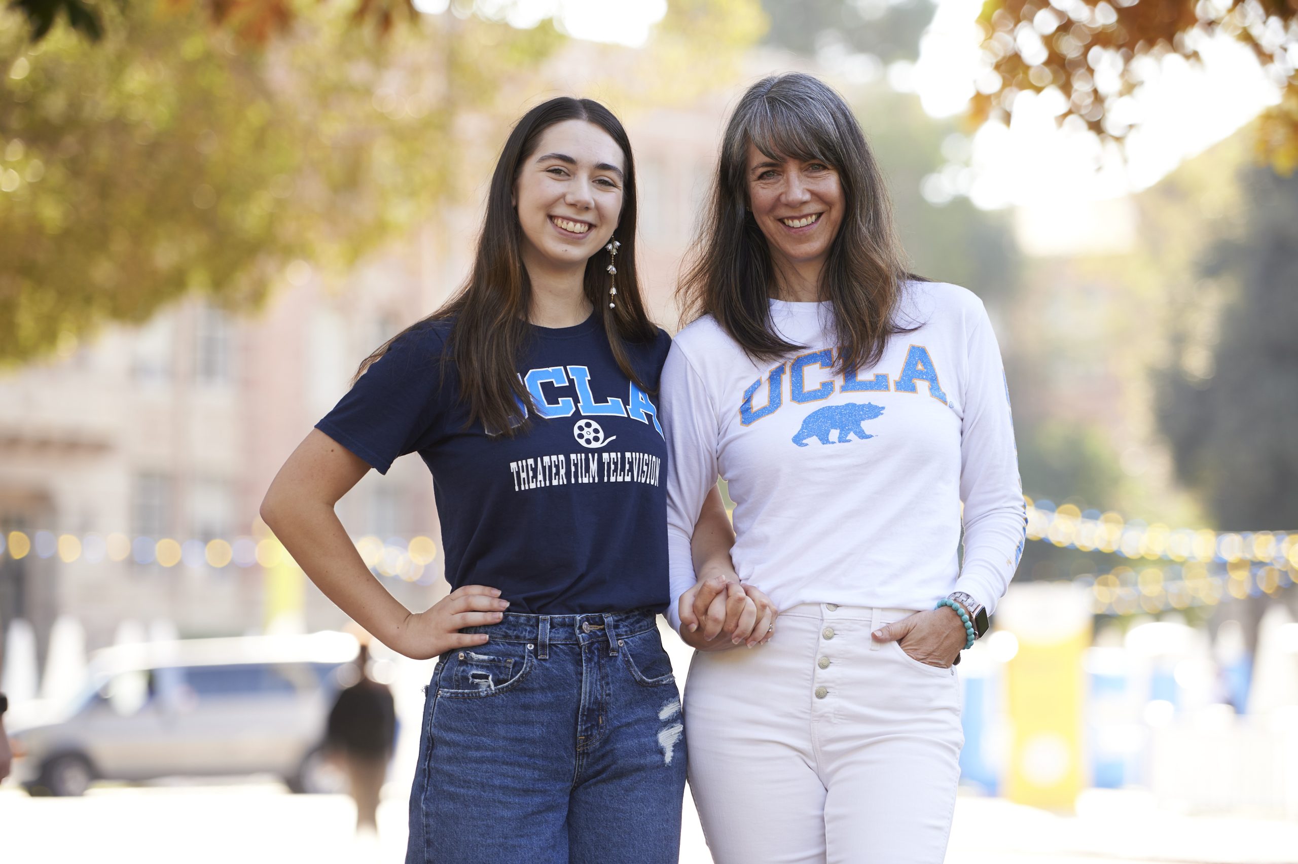A mother and a daughter hold hands wearing Bruin gear.